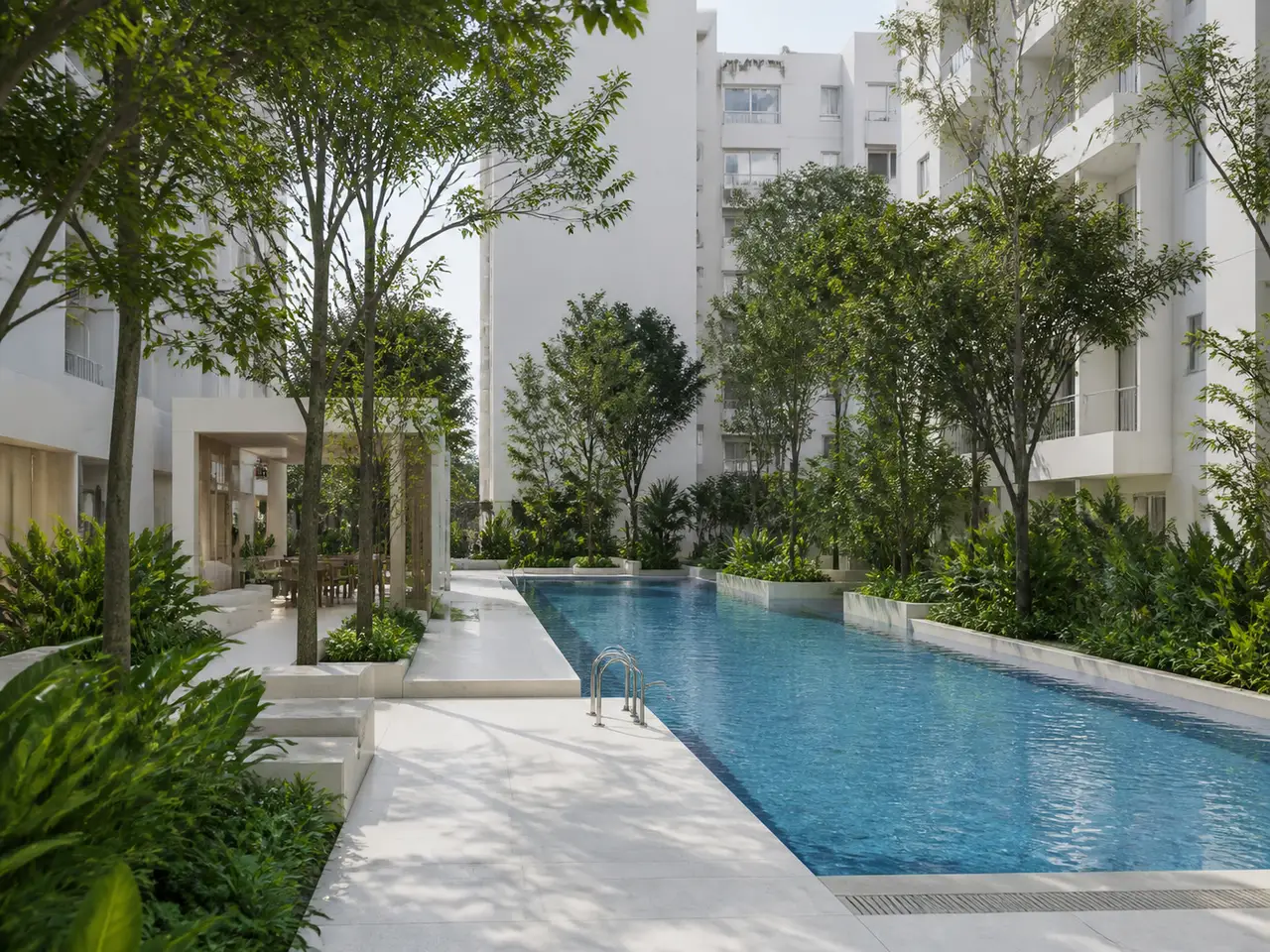 Outdoor lap pool between white apartment buildings and dense green planting